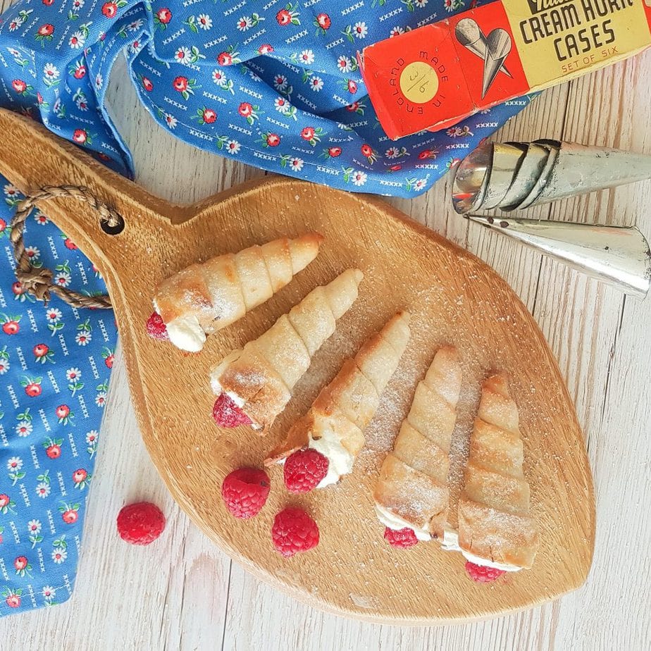 Gluten Free Cream Horns placed on a wooden pallette with vintage cream horn moulds in shot